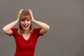 Young woman wearing red shirt standing over gray background with hand on head. Omg, shoked, surprised girl