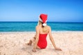 Young woman wearing Santa Claus hat on beach near sea, back view. Christmas vacation Royalty Free Stock Photo