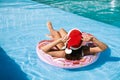 Young woman wearing Santa Claus hat on inflatable ring in swimming pool. Christmas vacation Royalty Free Stock Photo