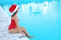 Young woman wearing Santa Claus hat near swimming pool, space for text. Christmas vacation Royalty Free Stock Photo