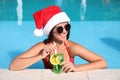 Young woman wearing Santa Claus hat with refreshing drink in swimming pool. Christmas vacation Royalty Free Stock Photo
