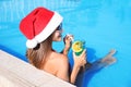 Young woman wearing Santa Claus hat with refreshing drink in swimming pool. Christmas vacation Royalty Free Stock Photo