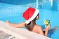 Young woman wearing Santa Claus hat with refreshing drink in swimming pool. Christmas vacation Royalty Free Stock Photo