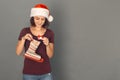 Christmas Time. Young woman in santa hat isolated on grey putting present into skate boot smiling joyful Royalty Free Stock Photo