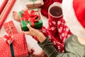 Young woman wearing santa hat and xmas pajamas sitting on the floor amongst wrapped christmas presents, drinking hot punch.