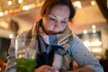 Young woman wearing scarf with drink in bright colourful cocktail bar using mobile phone looking at screen lighting up her face Royalty Free Stock Photo