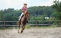 Young woman wearing shirt riding brown horse in sand paddock by wooden fence, hair moving in air because of speed Royalty Free Stock Photo