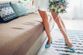 Young woman wearing silk dressing gown and blue shoes and holding bouquet at home. Morning of bride on wedding day Royalty Free Stock Photo