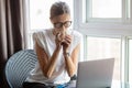 Young woman wearing smartwatch, drinking hot coffee and using laptop. Female working on computer pc at home during covid-19 Royalty Free Stock Photo