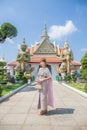 Young woman wearing traditional Thai dress stands holding an antique bag with giant front ornaments at the Wat Arun