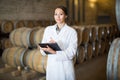 Young woman wearing uniform standing in large wine cellar