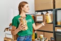 Young woman wearing volunteer uniform holding pasta jar at charity center Royalty Free Stock Photo