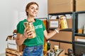 Young woman wearing volunteer uniform holding pasta jar at charity center Royalty Free Stock Photo