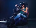 Young woman wearing VR headset having fun while driving on car racing simulator cockpit with seat and wheel.