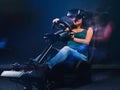 Young woman wearing VR headset having fun while driving on car racing simulator cockpit with seat and wheel. Royalty Free Stock Photo