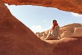 Young woman wearing warm jacket and scarf around head smiling, sitting at naturally formed rock window in Wadi Rum Valley of the Royalty Free Stock Photo