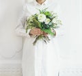 Young woman wearing white clothes holding bouquet, white wall background