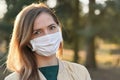 Young woman wearing white cotton virus mouth nose mask, blurred park and trees background, closeup face portrait, coronavirus