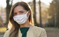 Young woman wearing white cotton virus mouth nose mask, blurred park and trees background, closeup face portrait, coronavirus