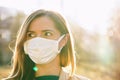 Young woman wearing white cotton virus mouth nose mask, nice backlight sun bokeh in background, closeup face portrait Royalty Free Stock Photo