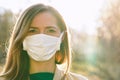 Young woman wearing white cotton virus mouth nose mask, nice backlight sun bokeh in background, closeup face portrait Royalty Free Stock Photo