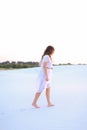 Young woman wearing white dress walking barefoot on sand. Royalty Free Stock Photo
