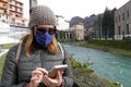 Woman wearing wool cap and medical mask using smartphone in the city on the river bank Royalty Free Stock Photo