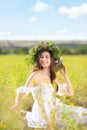 Young woman wearing wreath made of beautiful flowers in field on sunny day Royalty Free Stock Photo