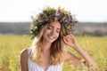 Young woman wearing wreath made of beautiful flowers in field on sunny day Royalty Free Stock Photo