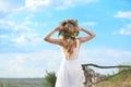 Young woman wearing wreath made of beautiful flowers outdoors on sunny day, back view Royalty Free Stock Photo