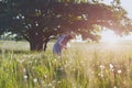 Young woman wearing yellow straw hat and long linen dress enjoying nature, picking fresh beautiful dandelions, hot summer sunny da Royalty Free Stock Photo