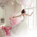 Young woman in wedding dress in luxury interior flies on pink and white balloons. Royalty Free Stock Photo
