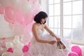 Young woman in wedding dress in luxury interior with a mass of pink and white balloons. Hold in hands her white shoes Royalty Free Stock Photo