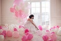 Young woman in wedding dress in luxury interior with a mass of pink and white balloons. Hold in hands her white shoes Royalty Free Stock Photo