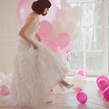 Young woman in wedding dress in luxury interior with a mass of pink and white balloons. Hold in hands her white shoes Royalty Free Stock Photo