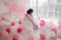 Young woman in wedding dress in luxury interior with a mass of pink and white balloons. Hold in hands her white shoes Royalty Free Stock Photo