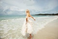 Young woman in wedding dress running over sea turning back. lucky and funny bride on the beach. Royalty Free Stock Photo
