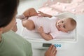 Young woman weighting her cute baby at home, above view. Health care Royalty Free Stock Photo