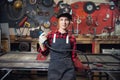 Young woman welder smiles and holds protective mask in hand on background industrial workplace or garage. Concept small