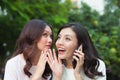 Young woman whispering into cheerful friend`s ear while on call Royalty Free Stock Photo