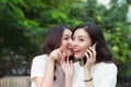 Young woman whispering into cheerful friend`s ear while on call Royalty Free Stock Photo