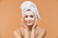 Young woman with white bath towel in her hair and mouisturizing face mask. Wellness and Spa concept on beige background. Royalty Free Stock Photo