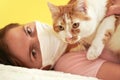 Young woman in white cloth virus face mask playing with her cat, detail on feline eyes, owner blurred in background