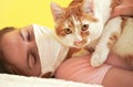 Young woman in white cloth virus face mask playing with her cat, detail on feline eyes, owner blurred in background