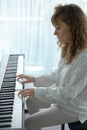 Young woman in white clothes sitting and playing an electronic piano Royalty Free Stock Photo