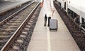 Young woman in white coat pulling her black trolley luggage behind on train platform, view from behind only anonymous lower part Royalty Free Stock Photo