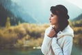 A young woman in a white coat walking in nature, looks away. Take cover from the autumn cold. Toned photo