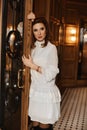 A young woman in white cocktail dress leans on the vintage door in the luxury interior Royalty Free Stock Photo