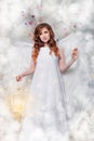 Angel in a white dress with angel wings holds in her hands a cage with magic light, standing in the clouds Royalty Free Stock Photo