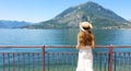 Young woman in white dress and hat looking blue water of lake and mountains on background